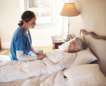 A caregiver sitting beside a smiling elderly woman resting in bed