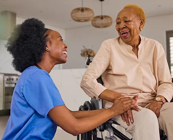 A caregiver laughing joyfully with an elderly woman in a wheelchair