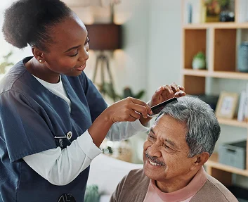 A caregiver combing the hair of a smiling elderly man at home
