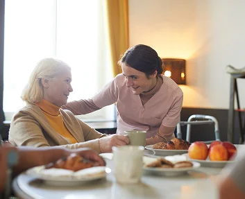 A caregiver serving coffee to a senior woman at a breakfast table