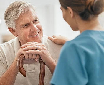 An elderly man with a cane smiling while speaking with a caregiver