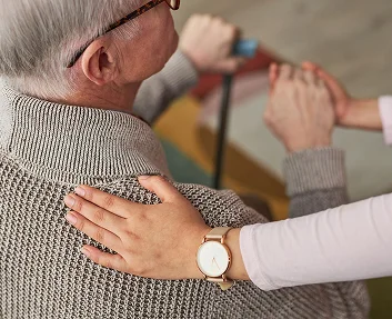 A caregiver gently placing a hand on an elderly person's shoulder from behind
