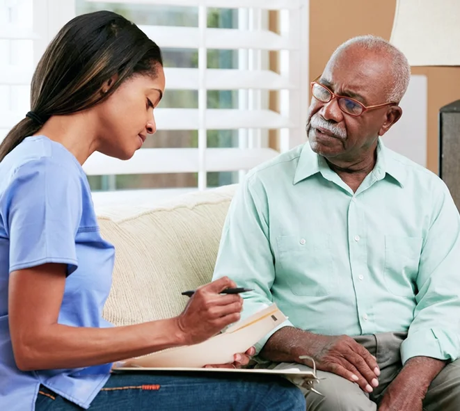 A caregiver taking notes on a clipboard while consulting with an elderly man
