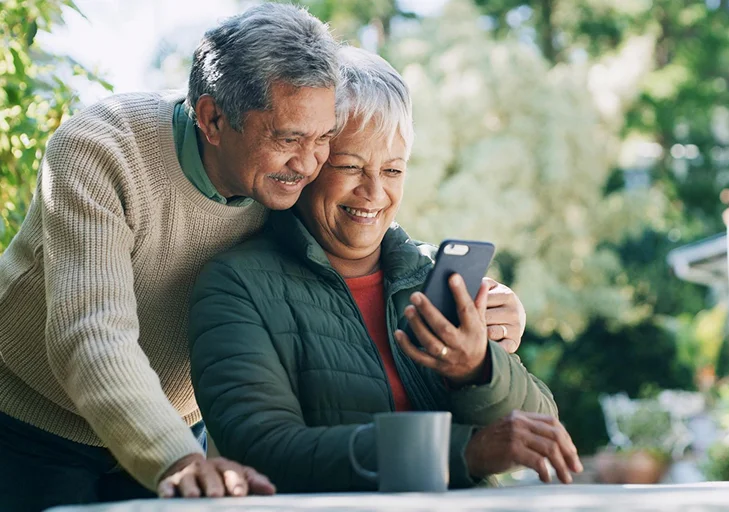 Senior couple smiling together at a phone outdoors