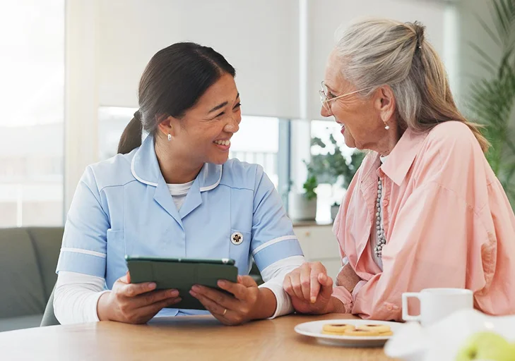 Nurse smiling with elderly woman at table