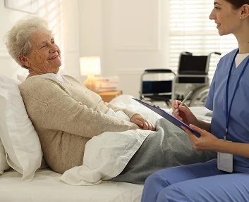Caregiver with clipboard speaking to smiling elderly woman in bed