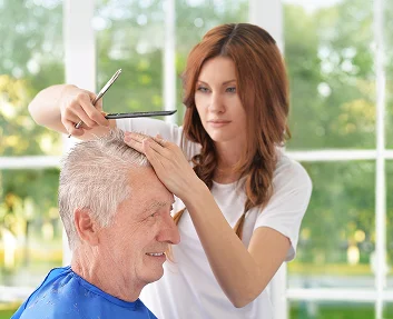 Caregiver cutting senior man's hair at home