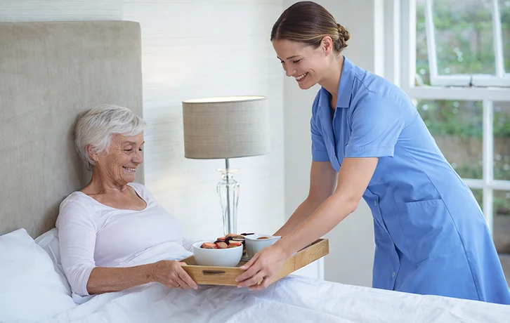 Caregiver serving meal tray to elderly woman in bed