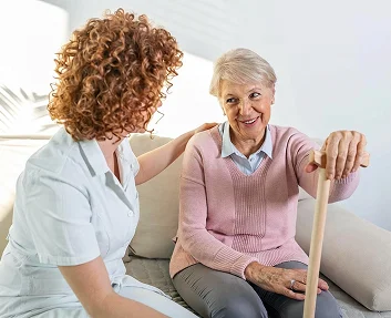 Caregiver sitting with smiling elderly woman holding a cane