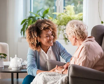 Caregiver holding hands with elderly woman in armchair