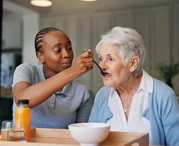 Caregiver feeding elderly woman at the table