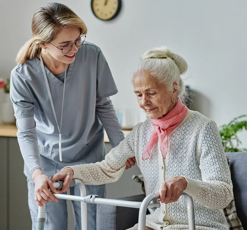 Caregiver helping elderly woman use a walker indoors
