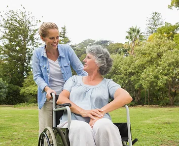Caregiver pushing smiling elderly woman in wheelchair outdoors