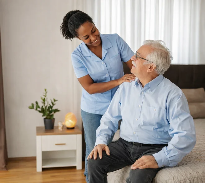 Caregiver smiling with seated elderly man in bedroom