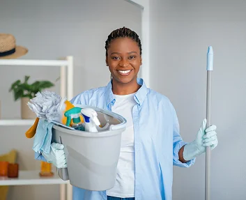 Smiling caregiver holding cleaning supplies and mop