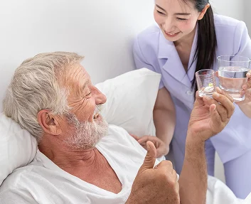 Caregiver offering water glass to elderly man in bed