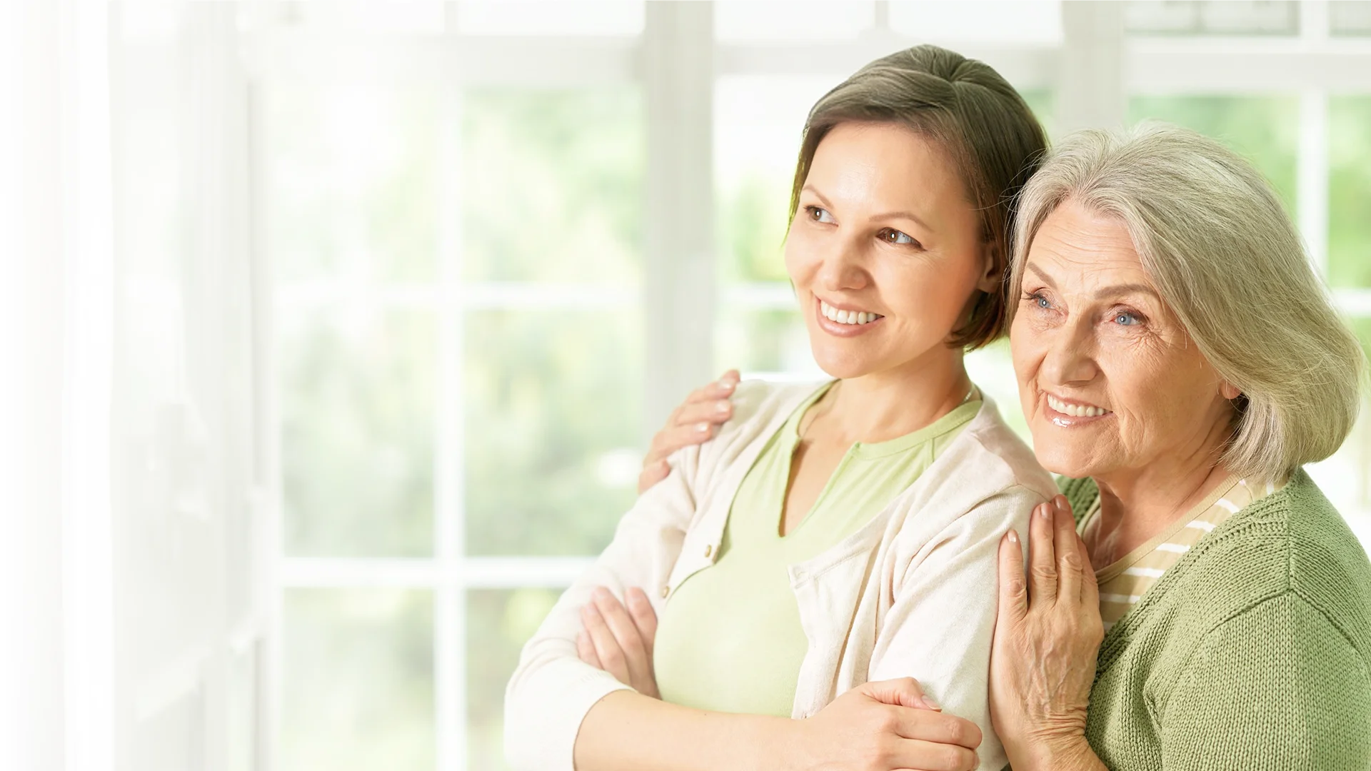 Adult daughter embracing elderly mother at home