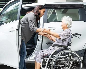 Woman assisting elderly wheelchair user from car