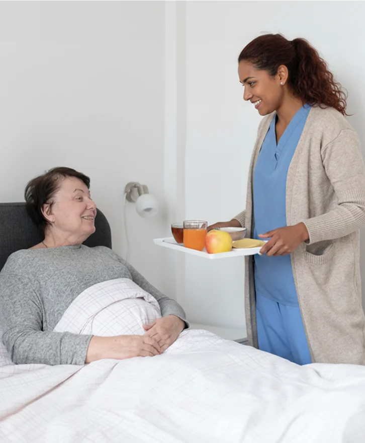 Caregiver serving a meal to a senior woman in bed