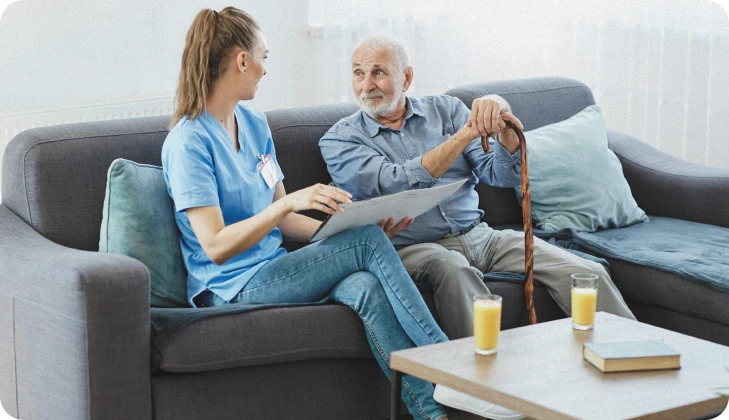 Caregiver discussing a care plan with a senior man holding a cane on a sofa
