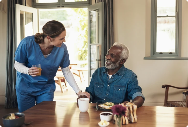 Caregiver serving juice to a smiling senior man at the breakfast table