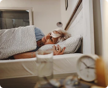 Senior woman resting in bed with an alarm clock on the nightstand