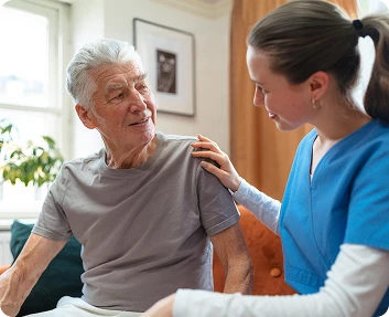 Caregiver in blue scrubs comforting a senior man with a hand on his shoulder