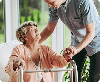 Caregiver helping a senior woman stand up using a walker at home