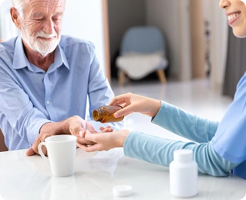Caregiver dispensing medication into a senior man's hand at a table