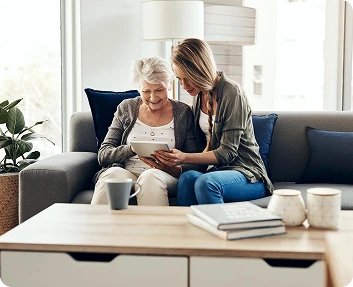 Caregiver and senior woman looking at a tablet together on a sofa