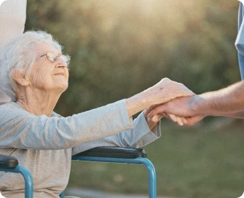 Claude responded: Senior woman in a wheelchair holding a caregiver's hand outdoorsSenior woman in a wheelchair holding a caregiver's hand outdoors