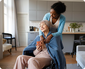 Caregiver wrapping a blanket around a senior woman in a wheelchair in a home kitchen