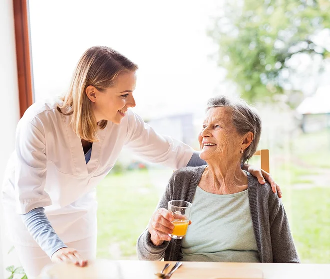Caregiver talking with an elderly woman holding a drink