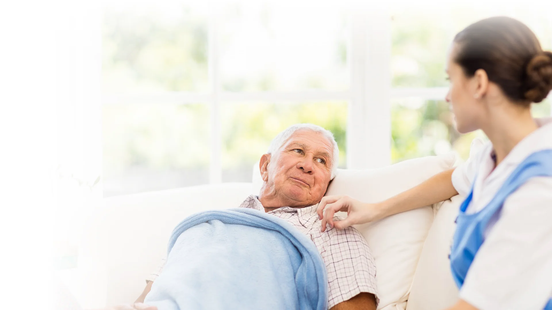 Caregiver talking with an elderly man resting in bed