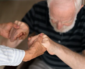 Caregiver holding elderly man's hands supportively