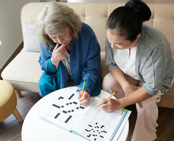 Caregiver and elderly woman doing a crossword puzzle together