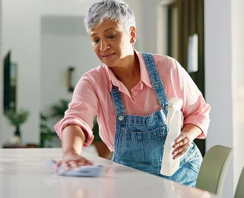 Older woman cleaning a table with spray bottle