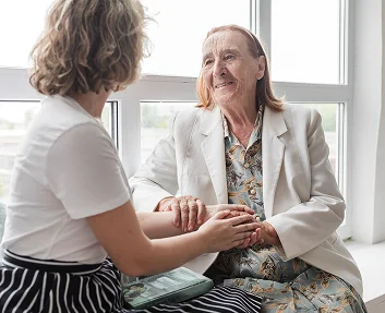 Caregiver holding elderly woman's hands by a window