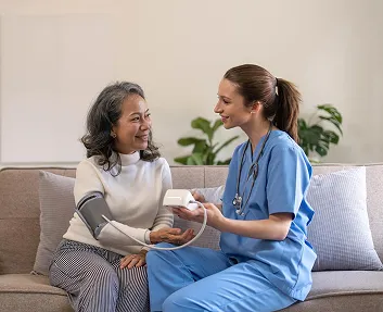 Nurse checking a senior woman’s blood pressure at home